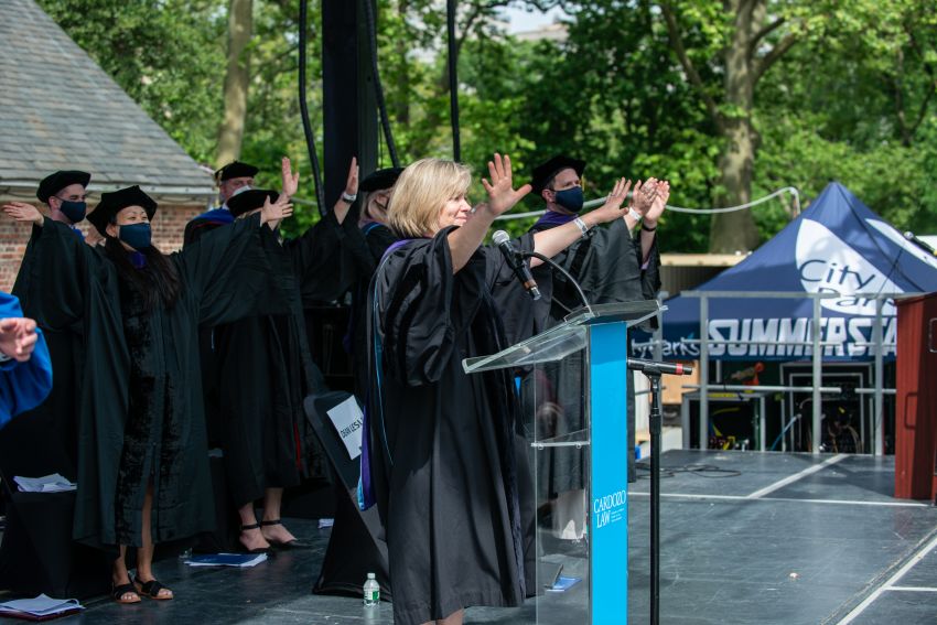 Dean Leslie at a podium with her arms outstretched 